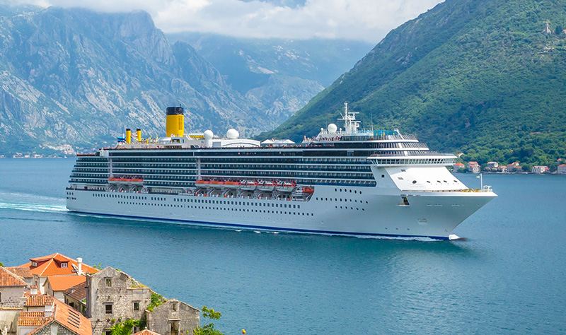 cruise ship in water, mountains and building in background and foreground