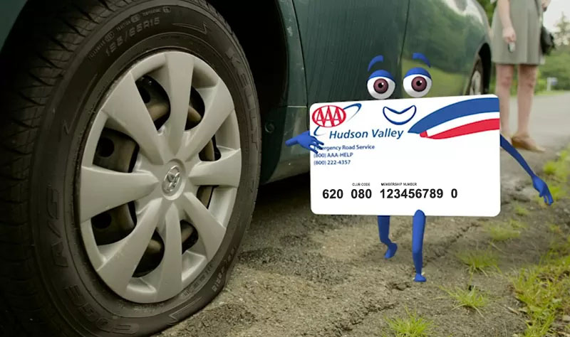 AAA card character standing next to car with flat tire